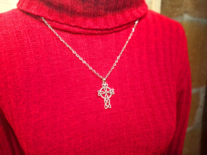 Pendentif croix celtique ajourée en entrelacs de triquètres, porté sur un pull en laine rouge à col roulé. Bijou La Blanche Hermine.